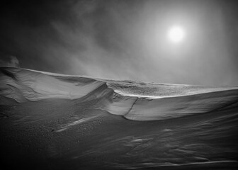 Grayscale shot of a white snow-covered mountain under a sunny sky