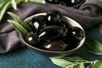 Bowl of tasty black olives on dark color background, closeup
