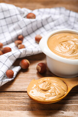 Bowl and spoon with tasty hazelnut butter on wooden background, closeup