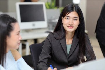 Attractive professional asian female employee worker sitting, using laptop computer and calculator with coworker at workplace. Businesswoman talking with coworker going over on new project together
