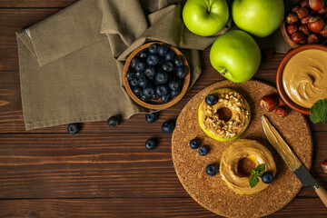 Cork mat of tasty apple rounds with nut butter, blueberry and hazelnuts on wooden table