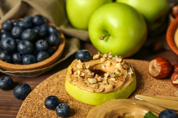 Cork mat of tasty apple rounds with nut butter on wooden table, closeup