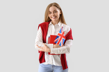 Young woman with UK flag and books on light background