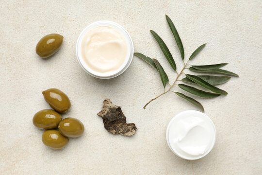 Jars of cream with green olives, plant branch and tree bark on white background
