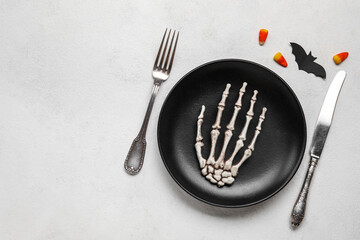 Table setting with skeleton hand in plate and Halloween decor on light background