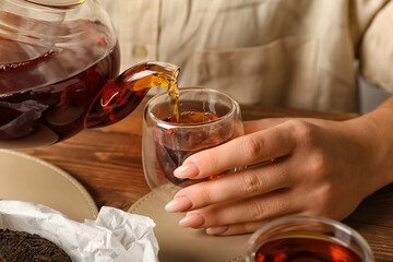 Woman pouring hot puer tea into cup at table, closeup