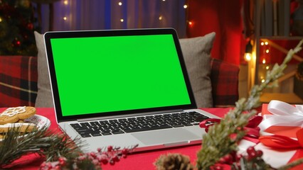 Green screen laptop standing on red table in room with christmas decorations. Place for...