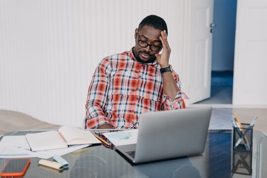 Upset tired african american man sitting at laptop solving working problems. Difficulties in job