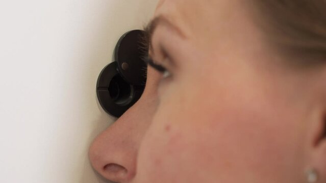 Woman looks through the peephole of the front door in the apartment. 