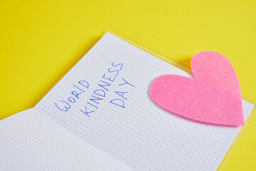 inscription world kindness day on notepad and felt heart on yellow background