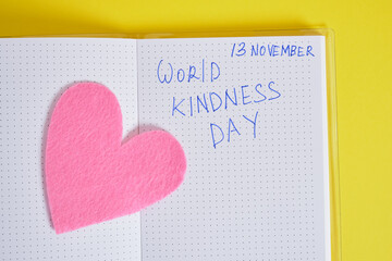 inscription world kindness day on notepad and felt heart on yellow background