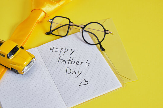 notepad with the inscription happy father's day, glasses, cars, tie on a yellow background, items in yellow colors