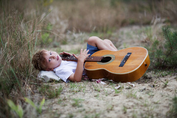 Chłopiec leży na trawie i gra na gitarze