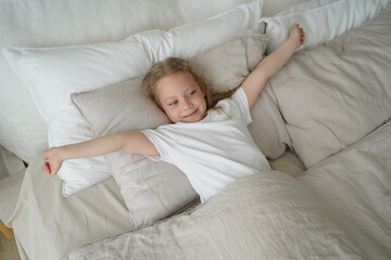Happy little child girl stretching, lying in soft bed after wake up. Healthy children's sleep