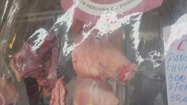 4k Video of a pig's head behind a plastic film in meat market. Camera tilts up. Other pig meat parts can be seen in the background of the butcher's shop.