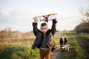 Chłopcy spełniają marzenie o lataniu, biegną drogą z samolotem w ręce - obrazy, fototapety, plakaty