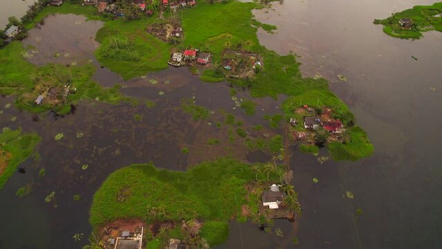 Drone flying forwards revealing several humble houses on lawns surrounded by water after flooding