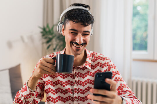smiling man drinking coffee and using mobile phone indoor