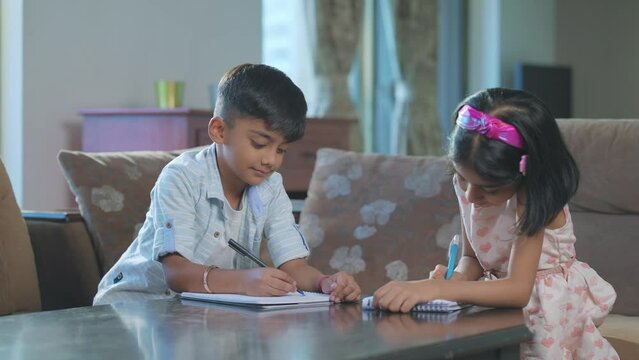 A modern Indian Asian adorable girl and a boy or a sister and brother busy writing or drawing on a notebook or notepad sitting in an interior home. study, Learning, education, homeschooling concept