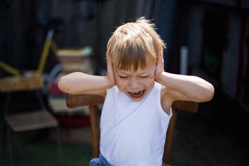 Rozgniewany chłopiec zakrywa uszy i krzyczy z przerażenia i bezradności