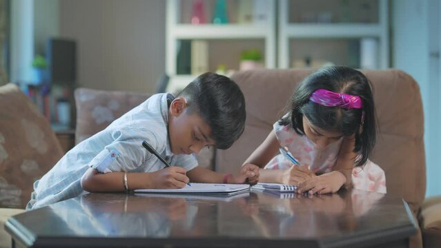 A modern Indian Asian adorable girl and a boy or a sister and brother busy writing or drawing on a notebook or notepad sitting in an interior home. study, Learning, education, homeschooling concept