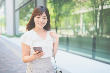 オフィス街でスマートフォンを持って歩くキャリアウーマン