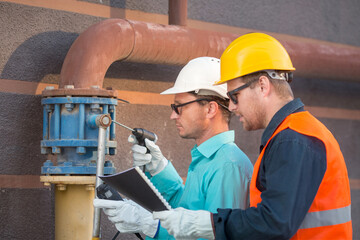 young men and a woman are standing near the gas pipe at the house with an analyzer and documents, checking the gas leak. Are they inspectors or engineers.