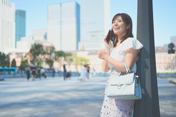 東京駅でスマートフォンを操作しながら待ち合わせをする若い女性