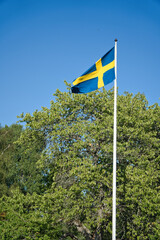 Sweden flag on flagpole on a farm in front of a tree in Smalland. blue, yellow flag