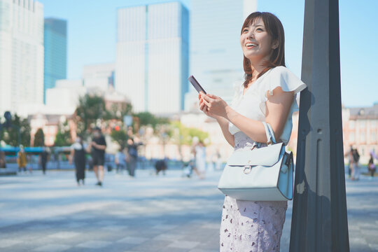 東京駅でスマートフォンを操作しながら待ち合わせをする若い女性