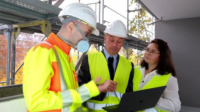 Two men, an architect and construction engineer, foreman and one woman inspect the performance of a project on a laptop, a construction site of a multi-storey house, building in progress