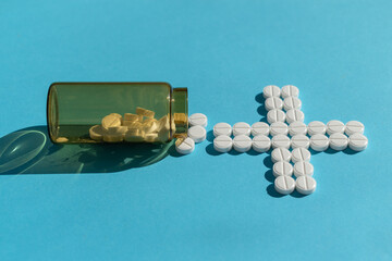 Medical background. On a blue background, a bottle of pills and a medical cross from pills. Side view. Treatment of the disease.