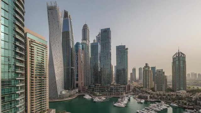 Dubai marina tallest skyscrapers and yachts in harbor aerial timelapse at morning with warm light. View at apartment buildings, hotels and office blocks, modern residential development of UAE