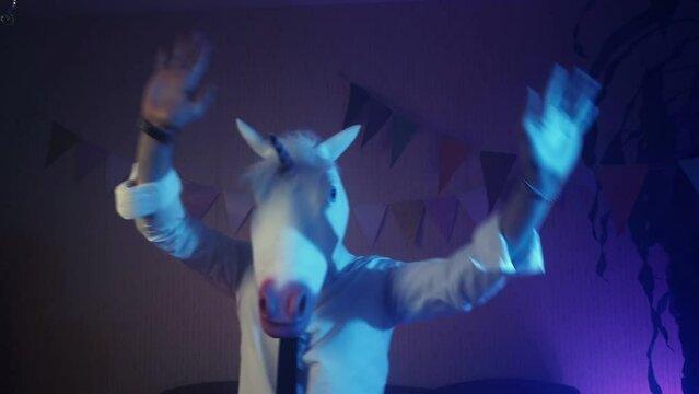 A young man in a unicorn mask is dancing. Multicolored lighting. Masquerade