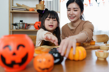 Fototapeta premium Young girl and mother at Halloween making treats and cupcake on table. Happy Halloween day