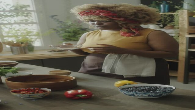 Close up tilt up shot of African American woman adding salt to ingredients in wooden bowl while preparing food in kitchen