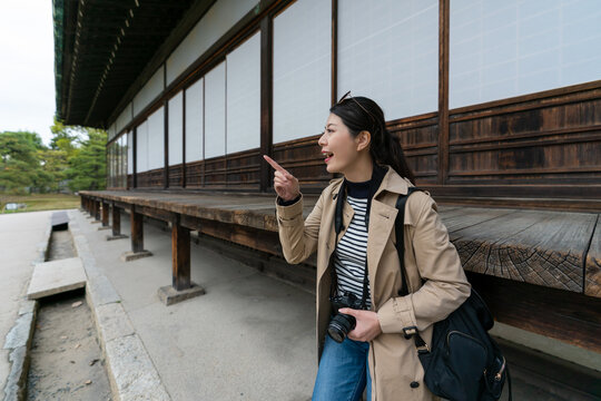 cheerful asian Japanese girl tourist noticing something fun at distance and finger pointing at it while standing by the wood veranda of imperial palace at nijo castle in Kyoto japan