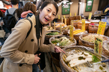 cheerful asian Japanese woman tourist smiling at camera and pointing at traditional preserved daikon at a local shop on teramachi dori at nishiki market in Kyoto japan