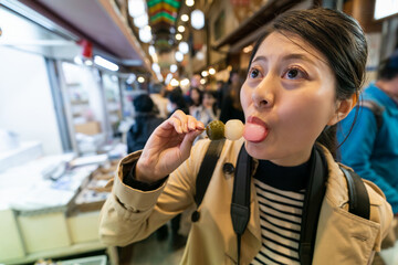 closeup portrait of asian Chinese female visitor biting into yummy Japanese dango with satisfied...