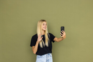 Young smiling happy woman do selfie shot on mobile cell phone post photo on social network isolated on plain olive green khaki background studio. People lifestyle concept