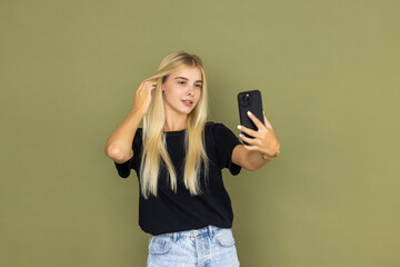 Close up young excited fun happy womandoing selfie shot pov on mobile cell phone hold face isolated on khaki background studio. People lifestyle concept
