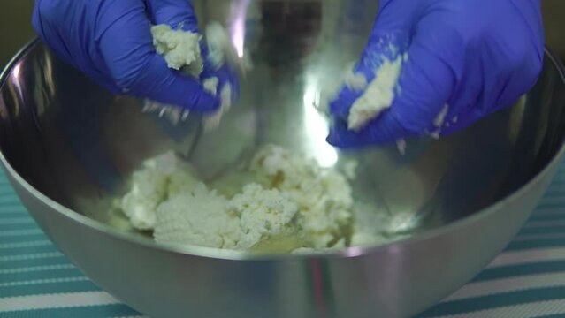 Cottage cheese making close-up with hands in gloves crushing cheese into pieces in a bowl