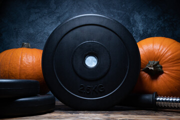 Heavy dumbbell barbell black weight plates with orange pumpkins. Healthy fitness lifestyle autumn fall composition for Halloween or Thanksgiving. Gym workout and sport training concept.
