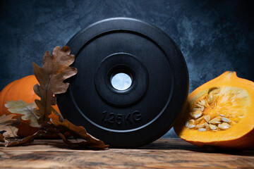 Dumbbell barbell weight plate with Hokkaido red kuri squash pumpkin and autumn leaves. Healthy...