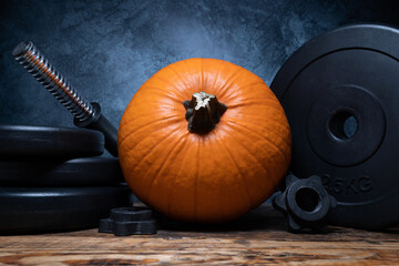 Orange pumpkin with heavy dumbbell barbell black weight plates. Healthy fitness lifestyle autumn...