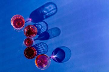 Red drink in tall and small glasses lined up on blue background. Party composition. Flat lay
