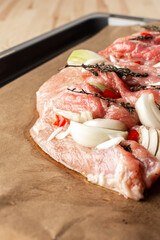 A large piece of raw pork meat prepared for baking, with onions and spices and thyme on parchment paper on a baking sheet