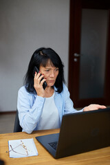 Senior woman talking speaking on phone on her workplace with laptop