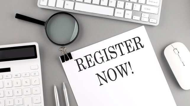 REGISTER NOW written on paper with office tools and keyboard on the grey background