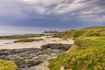 Clifftop view of the rock formations on Godrevy beach in Cornwall. In the distance under stormy skies is the Island with Godrevy Lighthouse